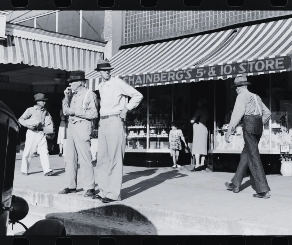 Black and White photo. People on a sidewalk outside of a store.