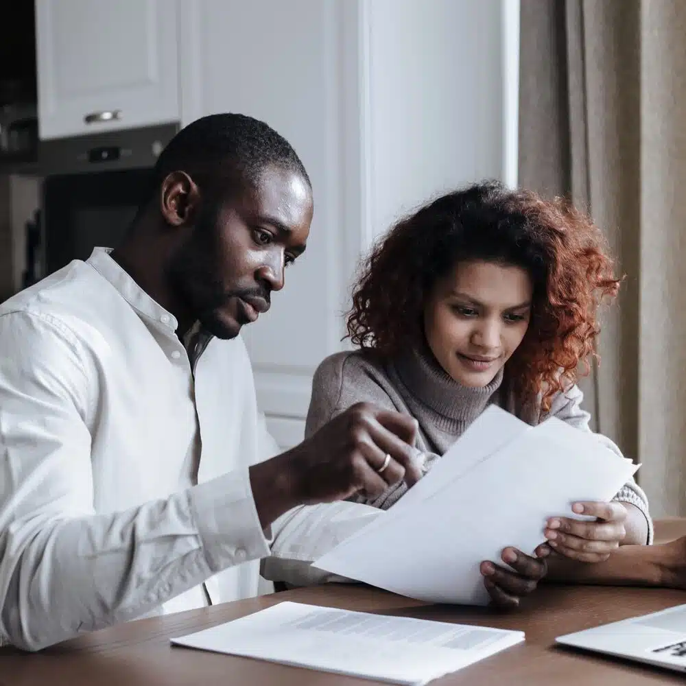 Loan Refinancing vs. Loan Modification: What’s the Difference? 1 Couple reviewing loan paperwork together at a kitchen table while comparing refinancing and modification options